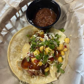 The Reckless Roadhouse - A taco topped with corn, chopped green onions, cheese, and sauce, served with a lime wedge and a small container of salsa. - New American Near Me - De Beque, Colorado