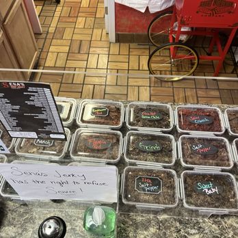 Sena's Beef Jerky - a variety of meats - Clear plastic containers with labeled beef jerky flavors are arranged on a counter at Sena's Beef Jerky shop, with a handwritten sign and a menu in the background. - Specialty Food Near Me - Albuquerque, New Mexico