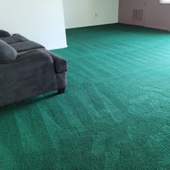 RK Carpet Services - High traffic area. - A living room features a dark gray upholstered sofa on a green carpeted floor, with a white wall and a window with curtains in the background. - Carpet Cleaning Near Me - Frederick, Maryland