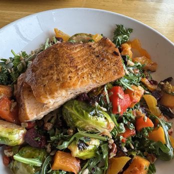 Silver Diner - Warm Roasted Local Veggie Salad with Grilled Fresh Salmon - A roasted salmon fillet is placed on a salad with mixed greens, roasted vegetables, and seeds, served on a white plate. - Diners Near Me - Lanham, Maryland