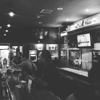 The Bit - a group of people sitting at a bar - Black-and-white image showing patrons seated at a bar in a sports bar, with sports memorabilia and TV screens on the walls. - Beer Bar Near Me - Arcadia, California