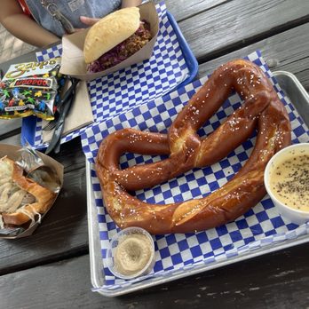 Scholz Garten - Giant pretzel with cheese, Bratwurst (left), and pork sandwich with chips. - German Near Me - Austin, Texas Scholz Garten - Giant pretzel with cheese, Bratwurst (left), and pork sandwich with chips. - German Near Me - Austin, Texas