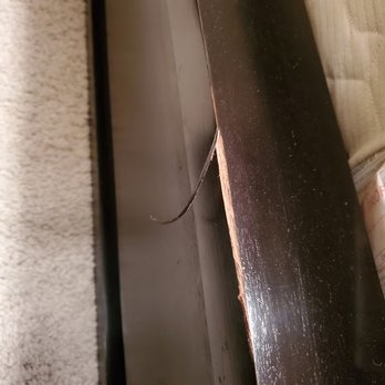 Vision Flooring - Damaged furniture. - The image shows a close-up of a wooden furniture item with visible damage, including a chipped edge. A loose wire extends from the back of the furniture, which is positioned near a carpeted surface. The setting appears to be indoors, possibly in a residential space, with the furniture placed against a wall. - Flooring Near Me - Chandler, Arizona