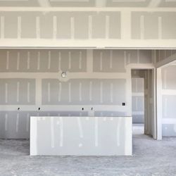 One Handy Haole - An interior room under construction shows newly installed gray drywall panels. The seams are taped and spackled with white jo...