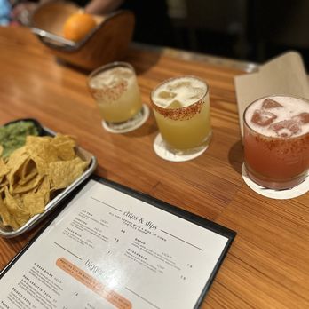 Lula - Three cocktails with salted rims are arranged on a bar counter, accompanied by a basket of bread and a menu, in a restaurant setting. - Cocktail Bars Near Me - Doylestown, Pennsylvania