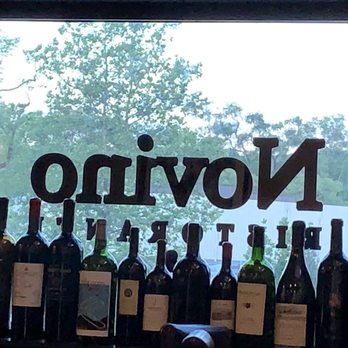 Novino - a row of wine bottles in front of a window - Italian Near Me - Mahwah, New Jersey
