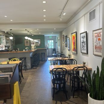 J.J. Hapgood General Store & Eatery - Indoor cafe area to enjoy prepared food and hot beverages - A cafe interior features wooden tables, black chairs, and framed artwork on white walls, with a bar area in the background. - Grocery Near Me - Peru, Vermont