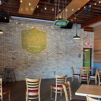 Beaver Island Brewing - Inside Beaver Island Brewing Co., a brick wall features a painted logo, with wooden tables and chairs arranged for patrons. Overhead lighting and a ceiling with exposed wood beams are visible. - Breweries Near Me - Saint Cloud, Minnesota