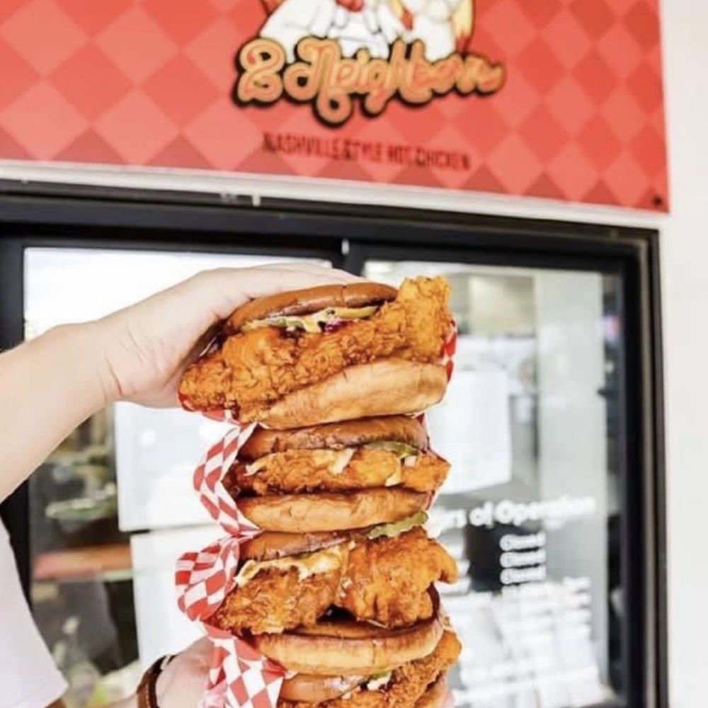 a person holding a stack of fried chicken sandwiches a person holding a stack of fried chicken sandwiches