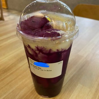 Matcha En - Taro Boba Tea - A boba tea with a purple and white swirl is served in a clear plastic cup with a domed lid, placed on a wooden table. - Desserts Near Me - Champaign, Illinois