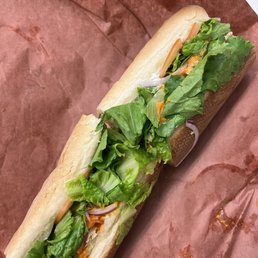 Buffalo Chicken Sub - A sandwich with fresh lettuce, tomato slices, and shredded vegetables in a white bread roll, placed on brown paper.