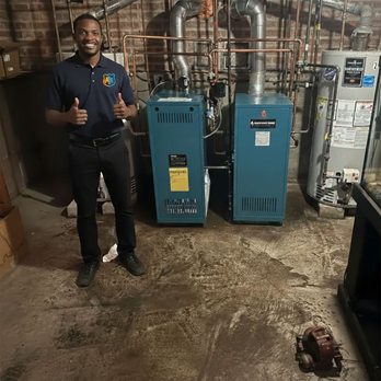 Frontline Heating & Cooling - HVAC technician standing beside newly installed residential boilers and water heater in basement mechanical room. - Heating & Air Conditioning/HVAC Near Me - Chicago, Illinois Frontline Heating & Cooling - HVAC technician standing beside newly installed residential boilers and water heater in basement mechanical room. - Heating & Air Conditioning/HVAC Near Me - Chicago, Illinois