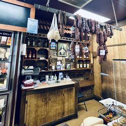 Late July 2026 - behind the counter. Dried sausages, caciocavallo (cheese), cold deli case.
