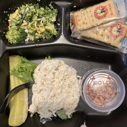 One scoop of chicken salad, a very small side of broccoli salad, with bacon bits on the side. A pickle and four crackers.