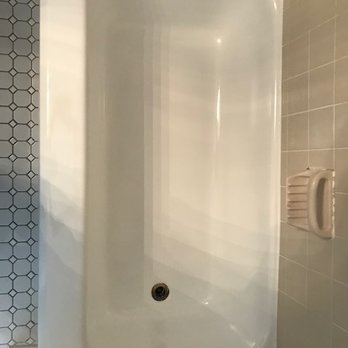 Bath Refinishing Solutions Cincinnati - A white bathtub with a smooth interior surface is installed in a bathroom, with tiled walls surrounding it. The drain is visible at the bottom of the tub, and a soap dish is mounted on the wall nearby. The tiles are light-colored, and the overall setting appears clean and well-maintained. - Refinishing Services Near Me - Cincinnati, Ohio