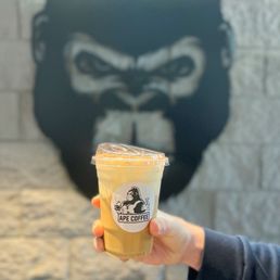 Tiramisu Latte | IG @moniquedao - A hand holds a plastic cup of iced coffee with a Gorilla logo in front of a Gorilla mural at Ape Coffee in Orange, CA.