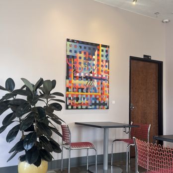 Strip Mall - Creative art throughout! - Indoor area featuring a large potted plant, a colorful abstract painting on the wall, and seating with red patterned chairs. - Coffee & Tea Near Me - Phoenix, Arizona