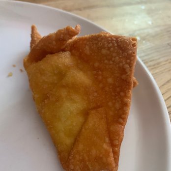 Chopsticks - a piece of fried food on a plate - A fried wonton with a crispy, golden-brown exterior is placed on a white plate. The background shows a wooden table surface, indicating a casual dining setting. The wonton appears to be freshly cooked, with a textured surface and slightly bubbled edges. - Chinese Near Me - Carpentersville, Illinois
