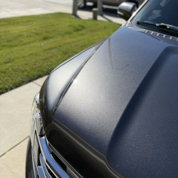 Caleb’s Auto Detailing - A black vehicle's front hood and grille are shown in a close-up, with a grassy area and other parked cars in the background. - Auto Detailing Near Me - Riverside, California
