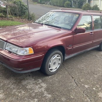 Eugene Car Care - Volvo 960 Wagon - A maroon Volvo 960 Wagon is parked on a concrete driveway in a suburban area with houses and greenery in the background. - Auto Repair Near Me - Eugene, Oregon