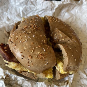 Springtree Bagels - Everything Bagel ( whole wheat) with bacon and scrambled eggs - A bagel sandwich with a whole wheat everything bagel topped with sesame and poppy seeds, filled with scrambled eggs and bacon. The bagel is cut in half, showing the filling inside, and is placed on crumpled white paper. - Bagels Near Me - Englewood, New Jersey