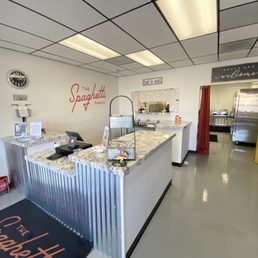 the kitchen and dining area - The image shows the reception counter of The Spaghetti Shack in Tempe, AZ, with a granite countertop, a cash register, and signage including the restaurant's name and welcome message.