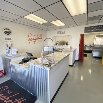 The Spaghetti Shack - the kitchen and dining area - The image shows the reception counter of The Spaghetti Shack in Tempe, AZ, with a granite countertop, a cash register, and signage including the restaurant's name and welcome message. - Italian Near Me - Tempe, Arizona