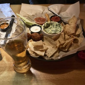 Applebee's Grill + Bar - Cold Combo appetizer and a stale coors light - A tray of Mexican appetizers features tortilla chips, guacamole, salsa, and chicken meatballs, served with small bowls of dips. A glass of beer is placed in front of the tray on a wooden table, with a person partially visible in the background. The presentation includes paper lining and various condiments. - Sports Bars Near Me - Turlock, California