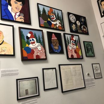 Graveface Chicago - Gacy Paintings - The wall features framed artwork of cartoon-style portraits, including clowns and a woman, along with framed documents and descriptions, in an art or museum setting. - Vinyl Records Near Me - Chicago, Illinois