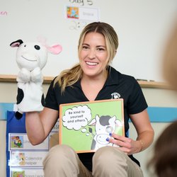 Primrose Schools preschool teacher reading character education book with cow hand puppet to young children