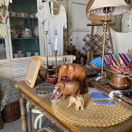 Vintage home decor items, including ceramics, wooden animal figurines, and lamps, are displayed on a wooden table in a thrift store setting.