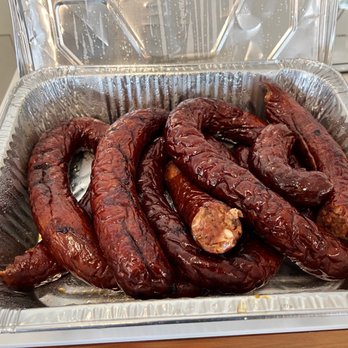 The Rub Bar-B-Que - Smoked Sausage - A foil tray contains several smoked sausages with a dark, glazed exterior, possibly from a barbecue restaurant or food service setting. - Barbeque Near Me - Olathe, Kansas