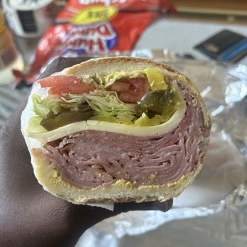Sam Deli - Italian sub - A cross-section of an Italian sub sandwich showing layers of deli meats, cheese, lettuce, tomato, and pickles in a sandwich bun. - Delis Near Me - Brooklyn, New York