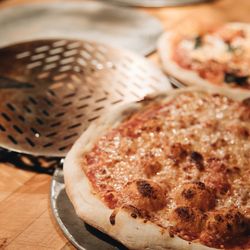A Margherita pizza in the foreground alongside freshly baked pizzas on the kitchen line, with a pizza peel nearby.