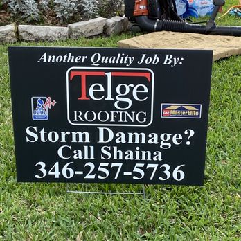 Telge Roofing - Day of the install, it took a team of 12 to start early and complete our roof by 3 pm.  Yard was spotless! - A black sign promoting Telge Roofing, highlighting storm damage repair services and providing a contact number, placed on a grassy area. - Roofing Near Me - Cypress, Texas