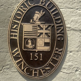 Hideaway Cafe - A metal oval emblem with the text 'Historic Building Winchester VA 151' mounted on a textured wall, featuring a crest with flags and a profile of a Native American figure. - Coffee & Tea Near Me - Winchester, Virginia