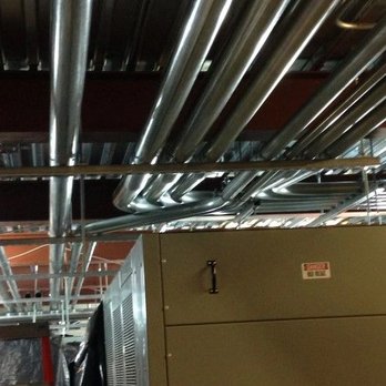 FS Electric - Large silver conduit pipes run organized across a ceiling, supported by metal racks. Below, a heavy-duty electrical unit labe... - Electricians Near Me - San Francisco, California