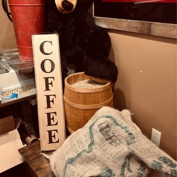 Eagle River Roasters - a stuffed bear and coffee sign - The image shows a plush bear head and paw, a coffee sign, a burlap sack, and a red watering can in a coffee shop setting. - Coffee Roasteries Near Me - Eagle River, Wisconsin