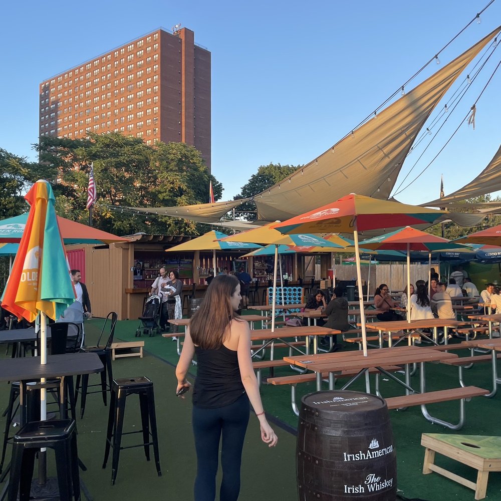 Fresh Pond Beer Garden - a woman standing in front of tables and umbrellas - Beer Gardens Near Me - Cambridge, Massachusetts Fresh Pond Beer Garden - a woman standing in front of tables and umbrellas - Beer Gardens Near Me - Cambridge, Massachusetts
