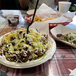 Carne Asada Burrito - A serving of carne asada fries with shredded cheese, sour cream, and green sauce on a white plate at a restaurant table.