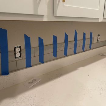 Pro Quality - Blue painter's tape marks the layout for a kitchen backsplash installation above the countertop, with electrical outlets visible. - Handyman Near Me