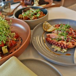 Fattoush Salad - The image shows Mediterranean cuisine with grilled octopus, salads, and garnishes on ceramic plates, presented on a dining table.