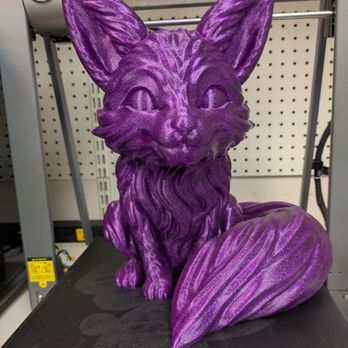Micro Center - 3d printed purple Fox - A purple glittery fox sculpture, 3D printed, is placed on a Creality 3D printer platform. The sculpture features detailed fur, large ears, and a bushy tail, with a shiny, glittery finish. It is situated in front of a pegboard wall with various equipment and tools visible in the background. - Computers Near Me - St Davids, Pennsylvania
