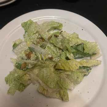 Michael J's - Side Cesar - A Caesar salad with chopped romaine lettuce, topped with croutons and grated cheese, is presented on a white round plate. The salad appears lightly dressed, and a lemon wedge is visible in a small metal container at the top of the image. The setting suggests a restaurant dining environment. - Italian Near Me - Ruidoso, New Mexico