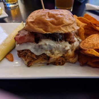 Jackson's Pit - Devin's Porkie Spice, a beautiful hot mess that tasted SO good!! - A burger with bacon, fried egg, and shredded meat on a bun, accompanied by potato chips and a pickle spear. - Burgers Near Me - Negaunee, Michigan