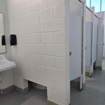 North Beach Park - The ladies!  Very sparkly and clean. - The image shows a public restroom with two sinks, each with a mirror and soap dispensers mounted on the wall. The walls are made of white bricks, and the floor is gray. There are multiple toilet stalls with doors, and the space is illuminated by natural light coming through windows with blinds. The restroom appears clean and well-maintained. - Parks Near Me - St. Augustine, Florida