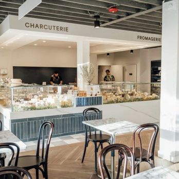 Nouvelle Maison - A cafe area inside a French-inspired shop features marble-topped tables, black chairs, and a display counter with cheeses and pastries. - Grocery Near Me - Winchester, Massachusetts