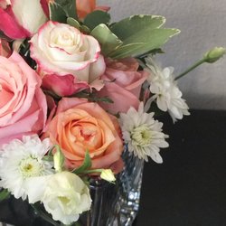 Blooms of Paradise - This modest centrepiece features peach roses, pink and white bicolour roses, white cushion mums, and pink roses in a crystal vase.
