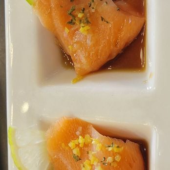 Hara Sushi - Yellowtail Asian pear - Two pieces of salmon sashimi are presented on a white rectangular plate, each topped with a small amount of garnish and drizzled with soy sauce. Lemon wedges are placed beside the sashimi for added flavor. The presentation emphasizes freshness and simplicity, typical of Japanese sushi dishes. - Sushi Bars Near Me - Grapevine, Texas