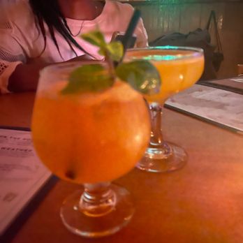 King Tai - Two colorful cocktails with garnishes are placed on a wooden table in a dimly lit setting, likely a bar or restaurant. - Cocktail Bars Near Me - Brooklyn, New York